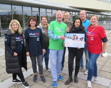 Martín Huber von der Regionalen Geschäftsleitung Süd der Deutschen Bank und Gabriele Nelkenstock von Verein „Hilfe im Kampf gegen Krebs“ (beide mit Plakat), umgeben vom am Uniklinikum Würzburg aktiven Projektteam der Deutschen Bank Region Süd.